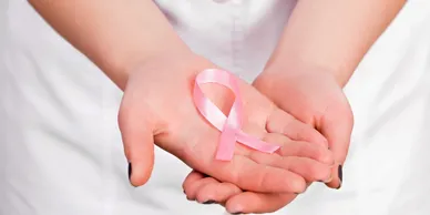 Hands holding a pink awareness ribbon.